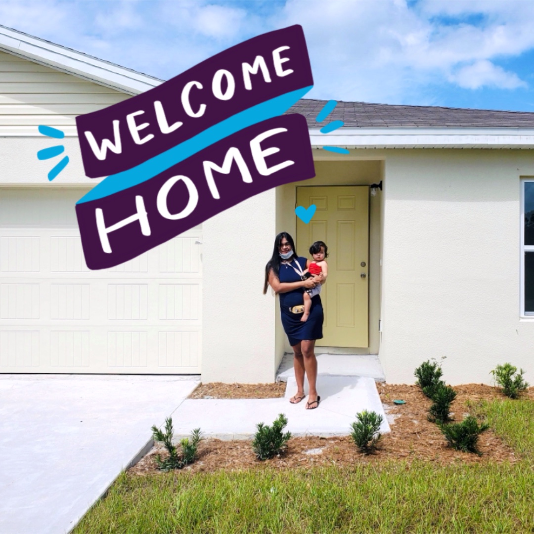 A person holding a baby in front of a house.