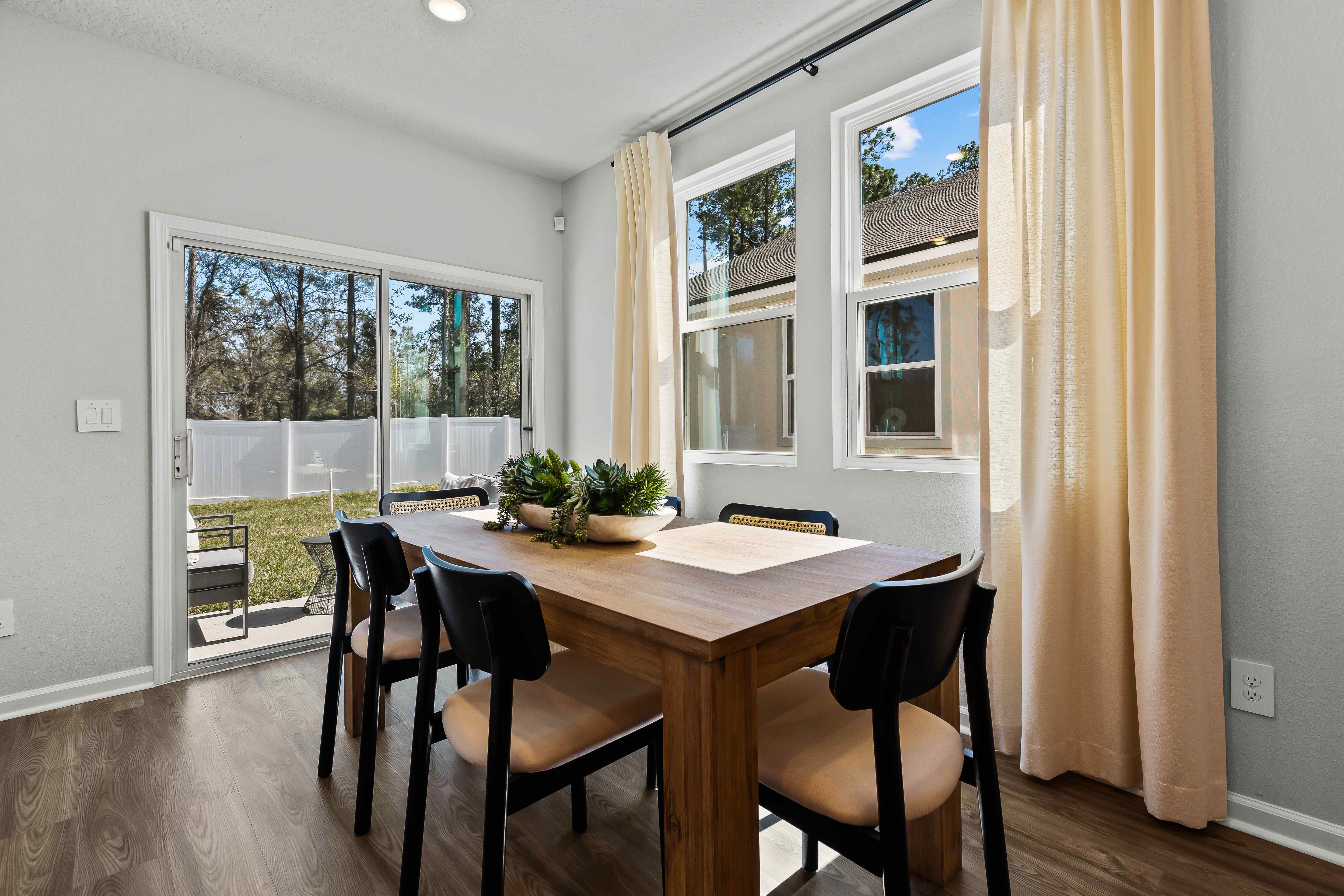 Davor Model Paired Home Dining Room with Wood Table and Black Chairs in Front of Patio Door at The Landings at Pecan Park