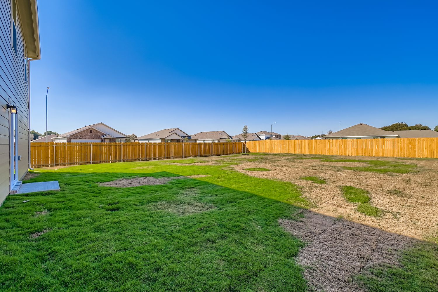 A fenced in yard with a dirt path and grass and a building.