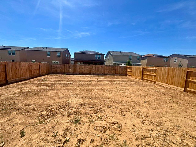 A dirt field with a fence and buildings in the background.